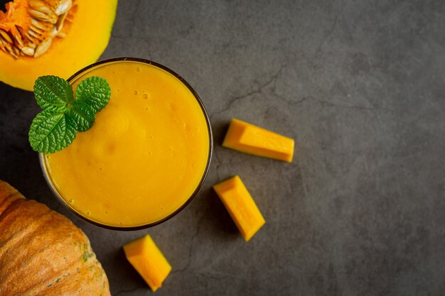 a glass of pumpkin juice and chopped raw pumpkins place on dark floor