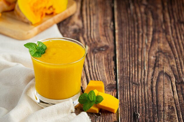 a glass of pumpkin juice and chopped raw pumpkins place on wooden  floor