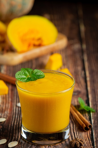 a glass of pumpkin juice and chopped raw pumpkins place on wooden  floor