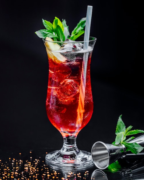 A glass of red drink with mint leaves and pipe.