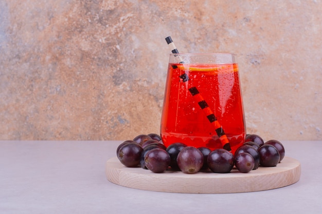 Free photo a glass of red juice with cherry berries on a wooden board