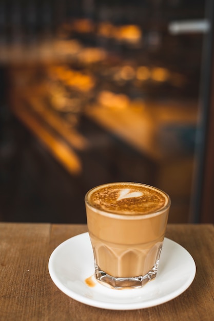 Glass of tasty latte with love art on wooden table in coffee shop