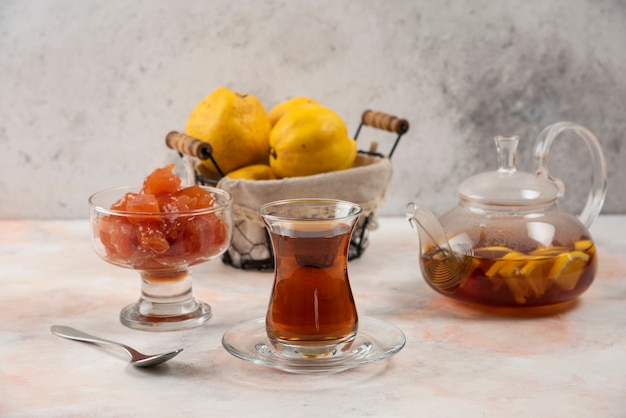 Free Photo glass of tea, jam and quince fruits on wooden plate. 