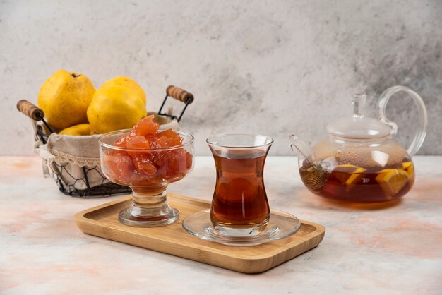 Glass of tea, jam and quince fruits on wooden plate. 