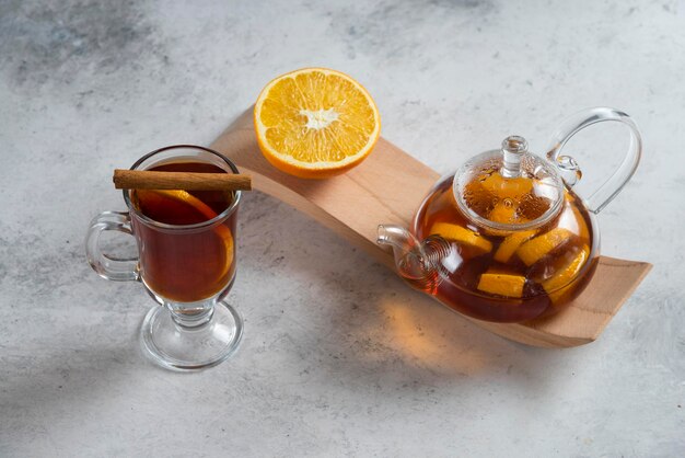 A glass teapot with tea and slice of orange.