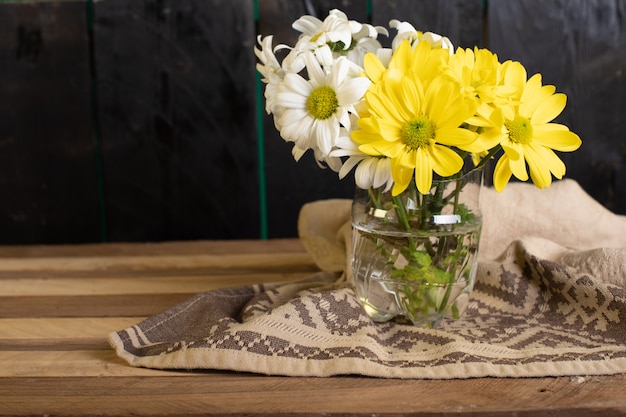 A glass vase of yellow and white flowers