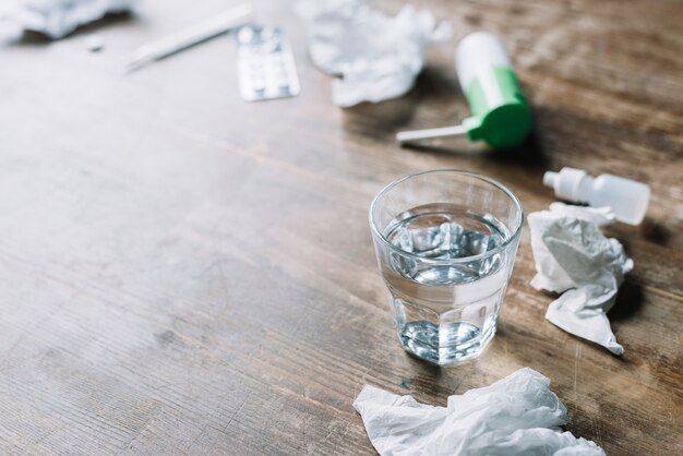 Glass of water; crumpled tissue paper and medicines on wooden backdrop