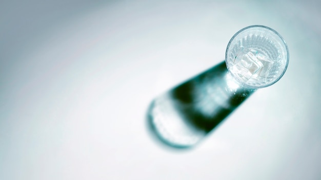 Glass of water with ice cubes and shadow on white background