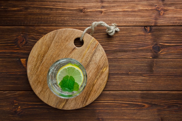 glass of water with lemon on wooden cutting board on wooden surface