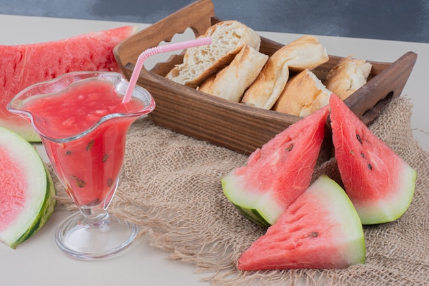 Free photo glass of watermelon smoothie and basket of bread on white table.