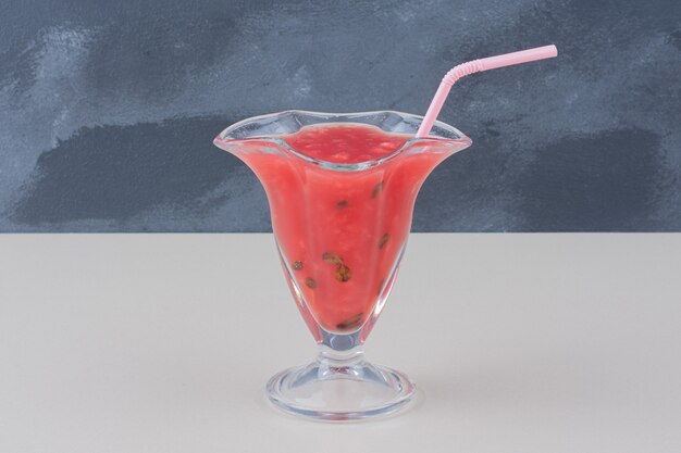 Glass of watermelon smoothie with straw on white table.