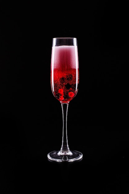 Glass with berries and red champagne alcohol cocktail stands on black background