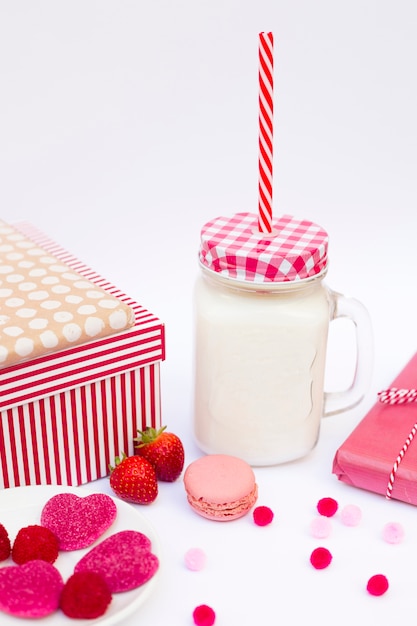 Glass with liquid and tube near biscuit, candies, berries and presents