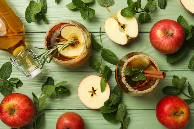 Free photo glasses and bottle with apple cider mint leaves and red apples on green wooden background top view