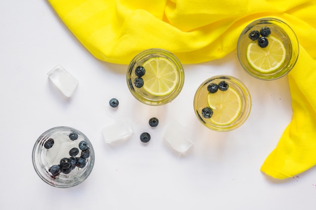 Free photo glasses of lemon juice and ice cubes with yellow fabric on white background