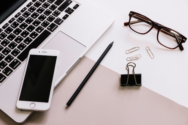 Glasses and stationery near smartphone and laptop