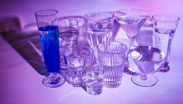 Glasses of water with blue cocktail on colored backdrop