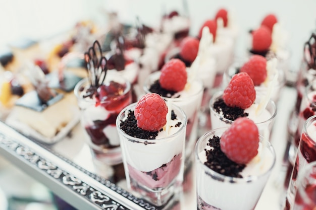 Free photo glasses with desserts of berries served on large mirror