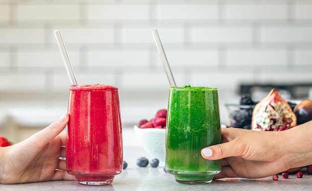 Free photo glasses with green and red smoothies in female hands on the kitchen table