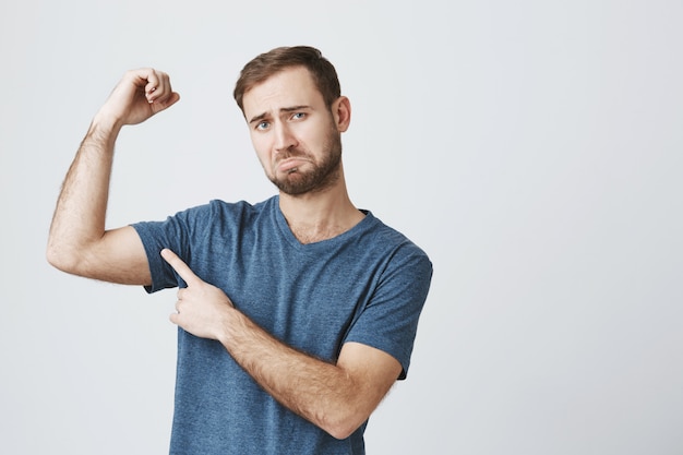 Free photo gloomy man complaining, flex biceps and frowning