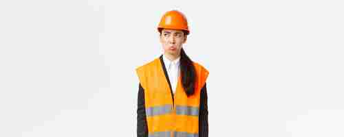 Free photo gloomy and offended young asian female construction manager industrial woman in safety helmet complaining or whining pouting sad and looking upper left corner disappointed