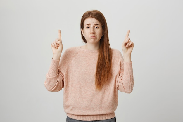 Free Photo gloomy upset redhead girl pouting indecisive, pointing fingers up