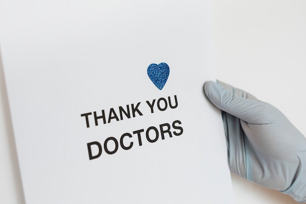 Free photo gloved hand holding a thank you doctors card during the covid-19 pandemic