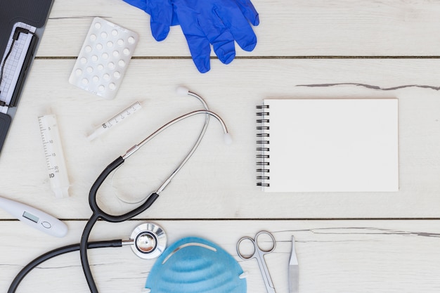 Gloves; pills; spiral notepad and medical equipment's on white wooden desk