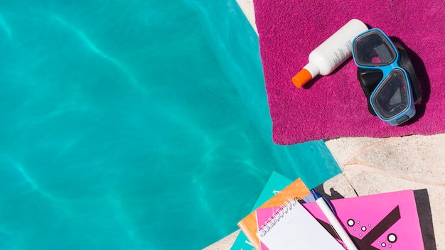 Goggles with lotion on towel near books and pool