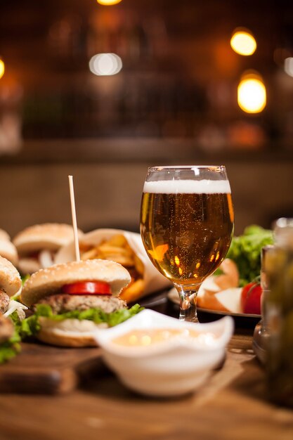 Golden beer next to delicious burgers on wooden table. French fries. Green salad. French fries. Garlic sauce.