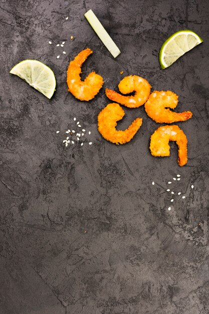 Golden fried shrimps with sesame seeds and lemon wedges over rough black surface