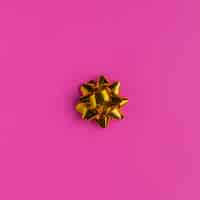 Free photo golden gift bow on bright pink background