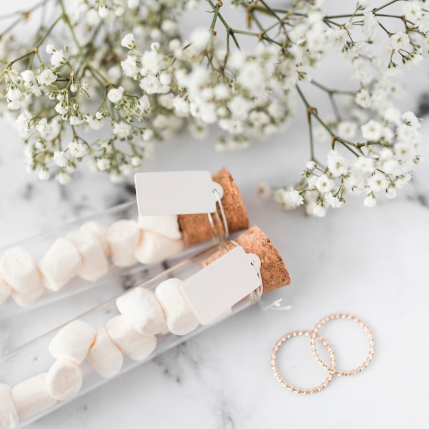 Free Photo golden wedding rings; baby's-breath flowers and marshmallow test tubes with white tag