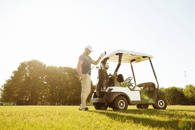 Free photo golfer taking clubs from a bag in a golf cart