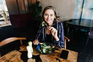 Free photo good-humoured caucasian woman enjoying healthy food. indoor shot of smiling girl eating salad.