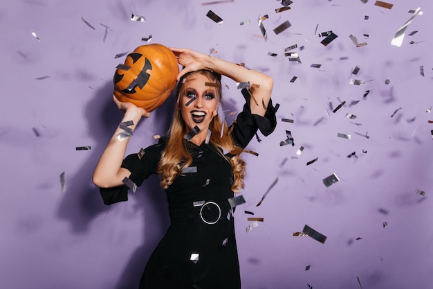 Good-humoured witch preparing for halloween. Happy blonde vampire dancing at party.