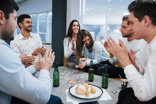 Good joke. Celebrating successful deal. Young office workers sitting near the table with alcohol