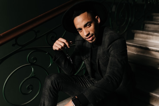 Free photo good-looking african man sitting on stairs and looking . tired guy in jacket posing on steps.