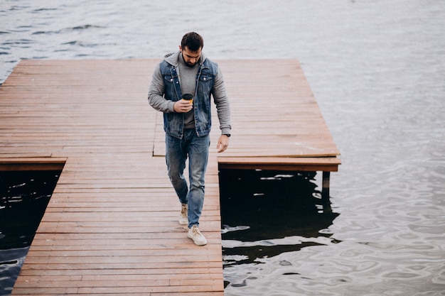 Free Photo good looking bearded man drinking coffee by the river in park