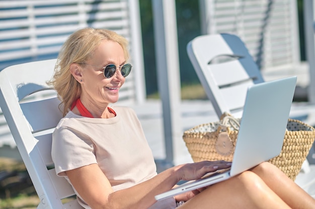 Free photo good-looking blonde woman with a laptop sitting in a chaise lounge