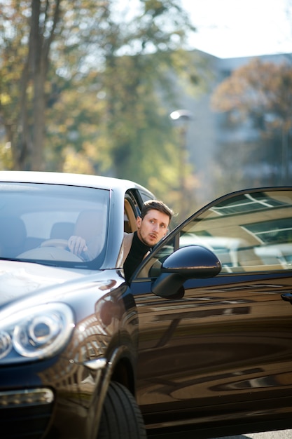 Good-looking caucasian driver is looking from the opened car door on the city street on a beautiful sunny day