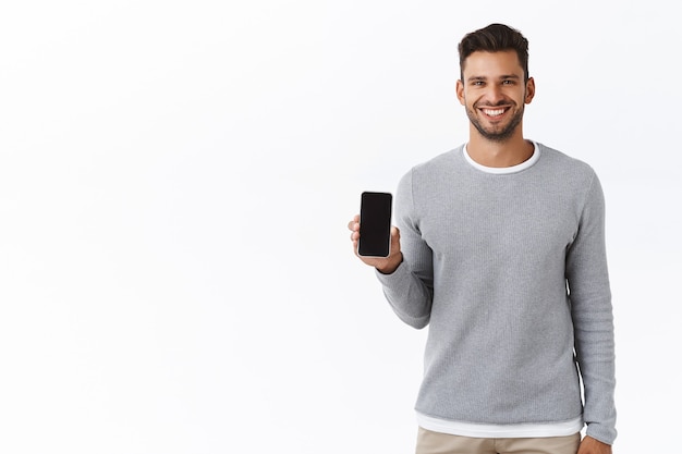 Free photo good-looking cheerful young man promote smartphone application, holding telephone or something on mobile screen, smiling satisfied