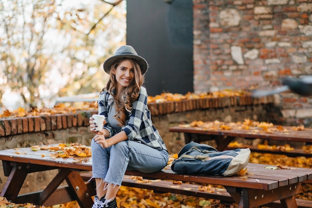 Free Photo good-looking girl in short denim pants sitting on wooden table in autumn park