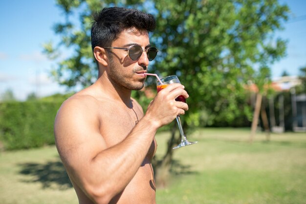 Good-looking man drinking bright cocktail. Man in sunglasses holding glass with bright beverage. Leisure, friendship, party concept