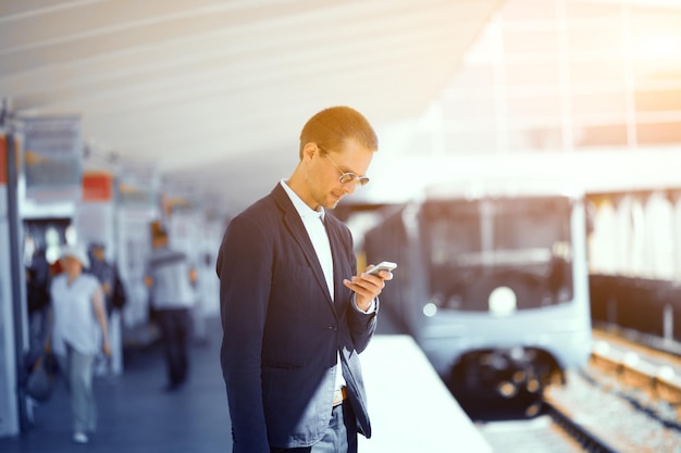 Free Photo good looking man in suit at metro station elegant young businessman standning at metro station looking at his cell with subway train blurred in background