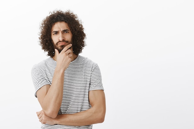 Good-looking masculine male sportsman with afro haircut, frowning and touching beard while making decision, being intense and focused during office meeting