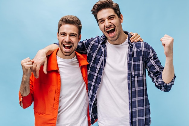 Goodhumored excited man in orange jacket and his friend in checkered shirt rejoice and scream on blue isolated background