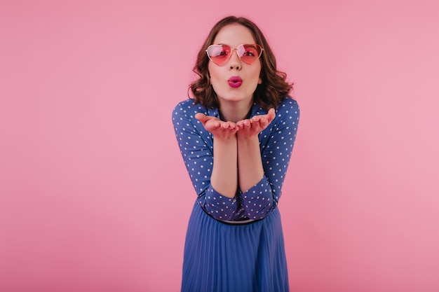 Free photo goodhumoured brunette girl sending air kiss while posing on pastel background lovely caucasian female model in blue clothes expressing positive emotions during photoshoot