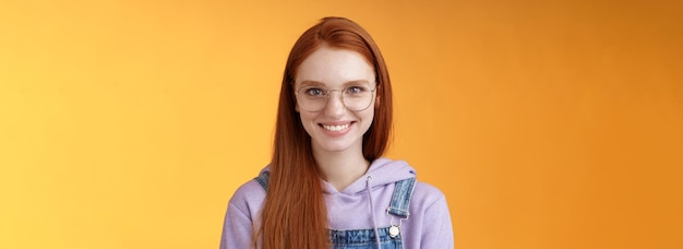 Goodlooking redhead female programmer glasses hoodie smiling satisfied look professional aim success standing confident grinning delighted camera talking casually orange background