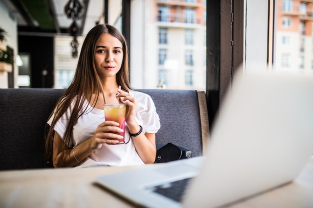 Gorgeous cheerful woman freelancer in a good mood, using laptop computer, sitting in cafes, sipping Mojitos.